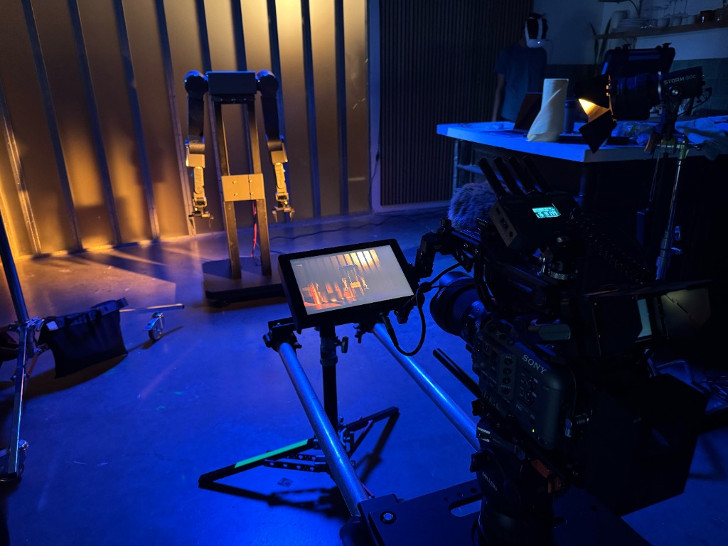 Cinema camera and monitor framing the lit AlmondBot robotic arm
