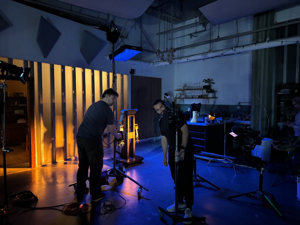 Crew adjusting lights and camera around the AlmondBot robotic arm on the dark set